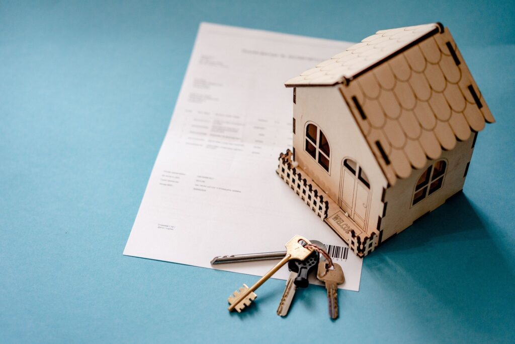 Una maqueta de una casa sobre un contrato en papel junto a unas llaves